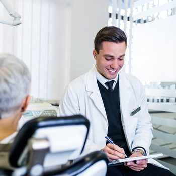 Handsome and attractive male dentist looking at dental x-ray together with his beautiful senior woman patient.