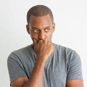 Pensive handsome young African man leaning on hand while thinking. Serious introspective guy in t-shirt focusing on problem. Reflecting concept