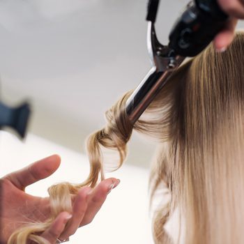 curling woman's hair giving a new hairstyle at hair salon close-up