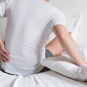 Rear view of one man sitting on bed having back pain