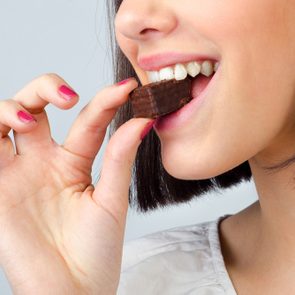 Portrait of the beautiful girl eating chocolate cookies isolated on gray background.