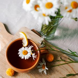 Herbal tea with fresh chamomile flowers in a ceramic mug on a linen tablecloth