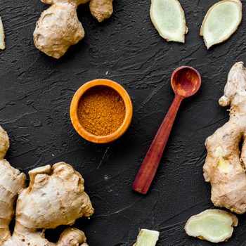 Seasoning. Ground ginger in small bowl near sliced ginger root on black background top view