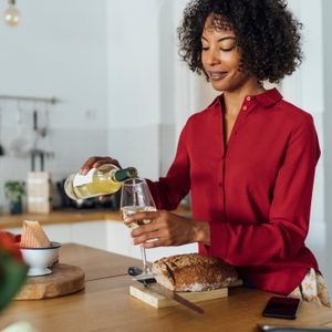 Woman standing in kitchen, pouring herself a glass of white wine