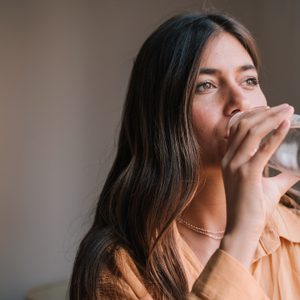 Beautiful Young Woman Drinking Water In Glass Bottle By Window