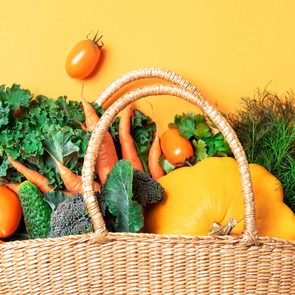 Straw basket with organic vegetables over trendy yellow background. Healthy food, vegetarian diet. Eco friendly, zero waste, plastic free concept.