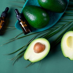 Avocado oil in dropper bottle and avocados on the green background