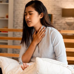 Portrait of 20s young Asian woman suffering pain and medical sickness in bedroom at night. Sore Throat, neck related pain symptoms