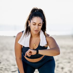 woman running on the beach stoops to check her heart rate on her watch