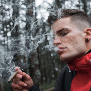 Young Man Smoking weed Standing In Forest During late Autumn