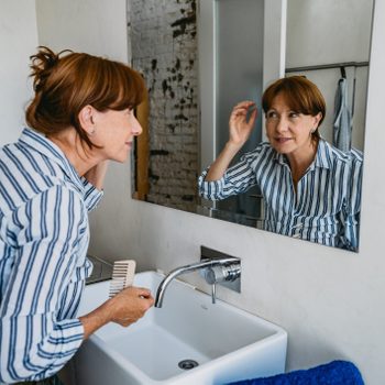 Senior Woman Adjusting Hair In Bathroom